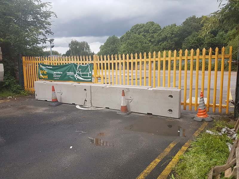 Concrete barriers and cones blocking a gateway in a yellow palisade fence