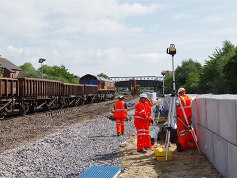 Rail workers surveying beside a Legato block wall next to a freight train