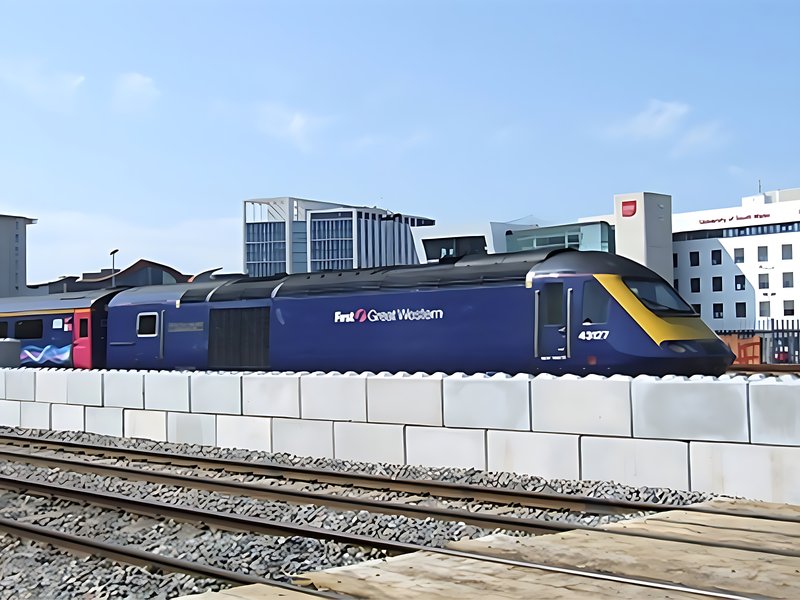 Passenger train running past a Legato interlocking block wall beside the track