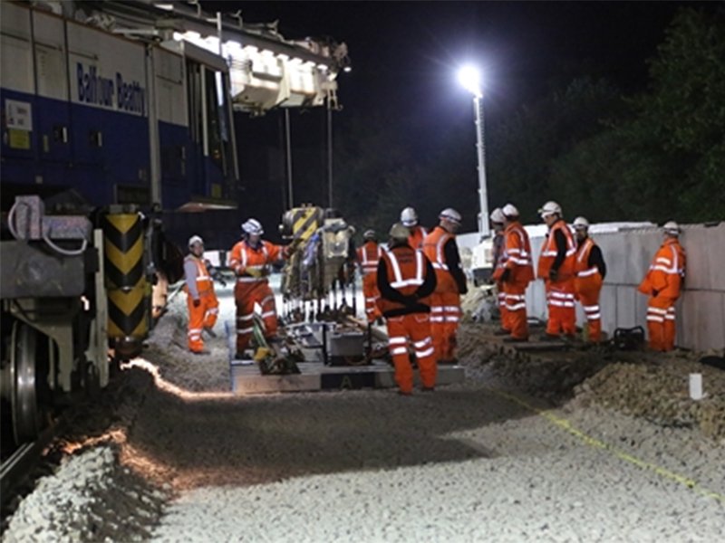 Night shift rail crew in orange PPE working beside stacked interlocking blocks