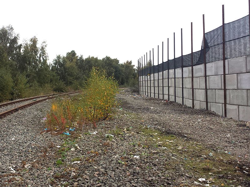 Trackside interlocking block wall topped with mesh fencing beside a railway line
