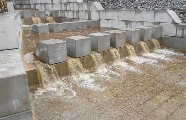 Water cascading over a stepped concrete block weir below a railway embankment