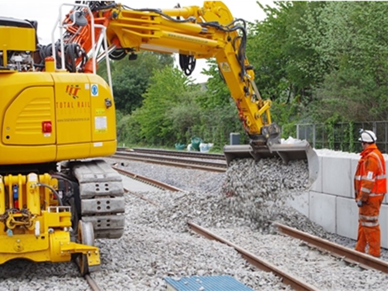 Rail-mounted excavator placing an interlocking block beside the track
