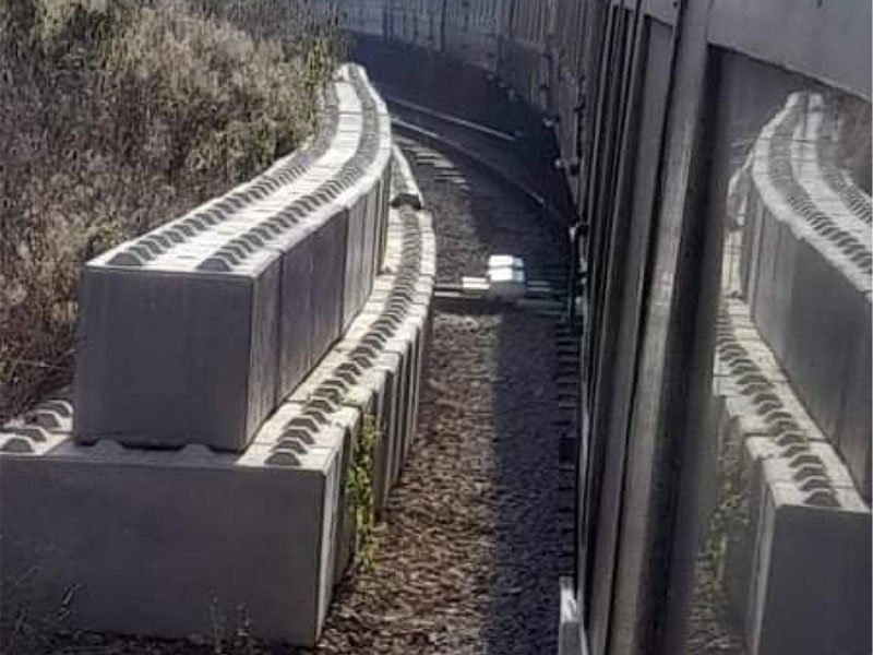 Interlocking blocks forming a curved safety wall against dark corrugated cladding