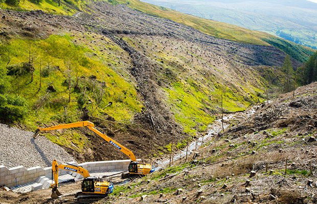 Excavators placing interlocking blocks along a hillside railway cutting