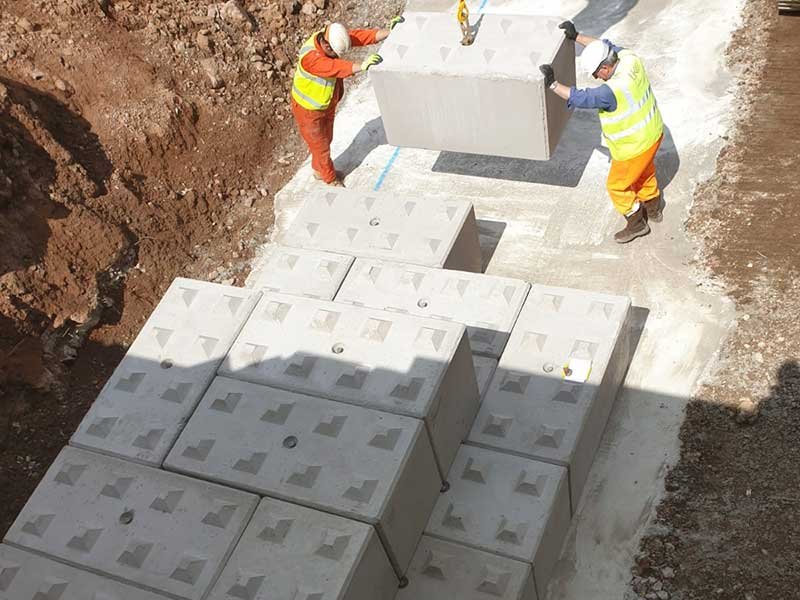 Workers guiding an interlocking block into place on a laid block base