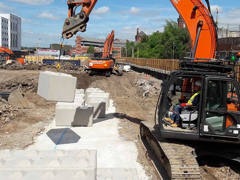 Excavator lifting an interlocking block into place on an urban construction site