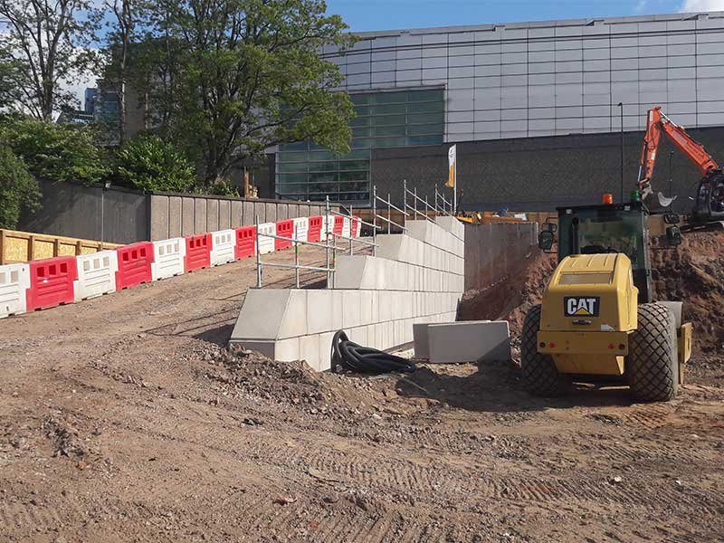 Line of interlocking blocks being built across a barriered construction site