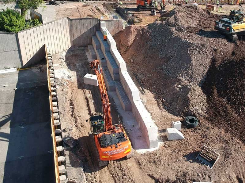Excavator working between interlocking block retaining walls and a spoil heap