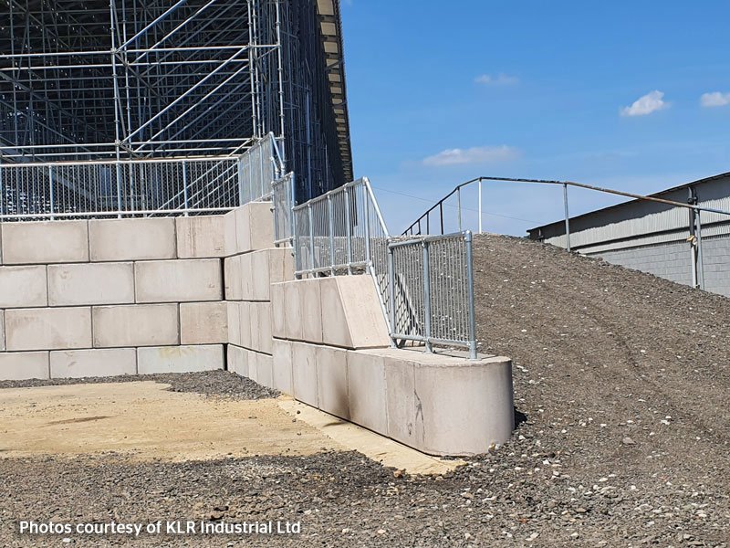 Interlocking block wall with mesh fencing beside a gravel access ramp