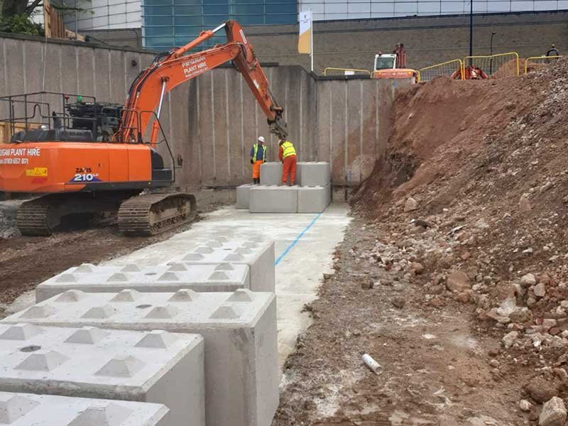 Excavator positioning Legato blocks in a trench beside an excavated earth bank
