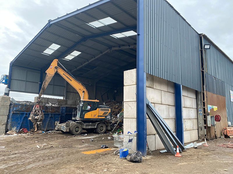 Excavator sorting scrap in an open-fronted shed with block push walls