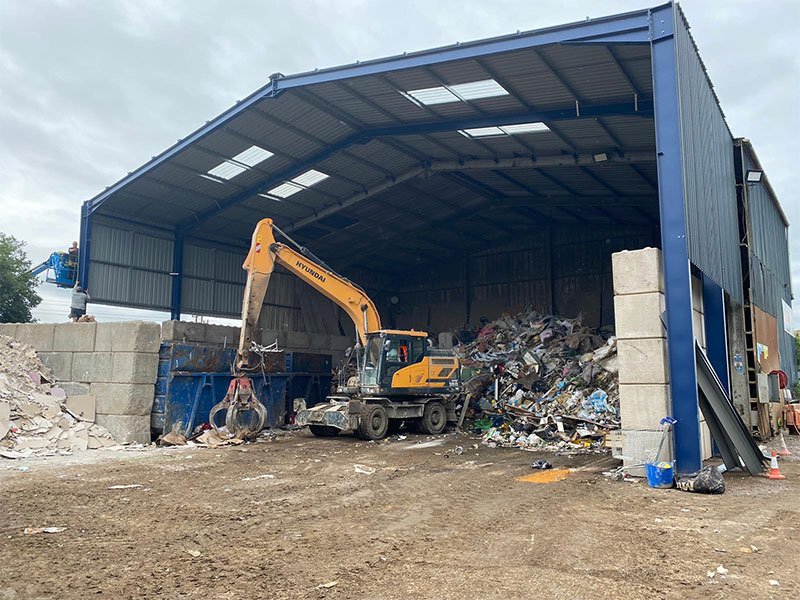 Material handler working scrap between interlocking block bay walls