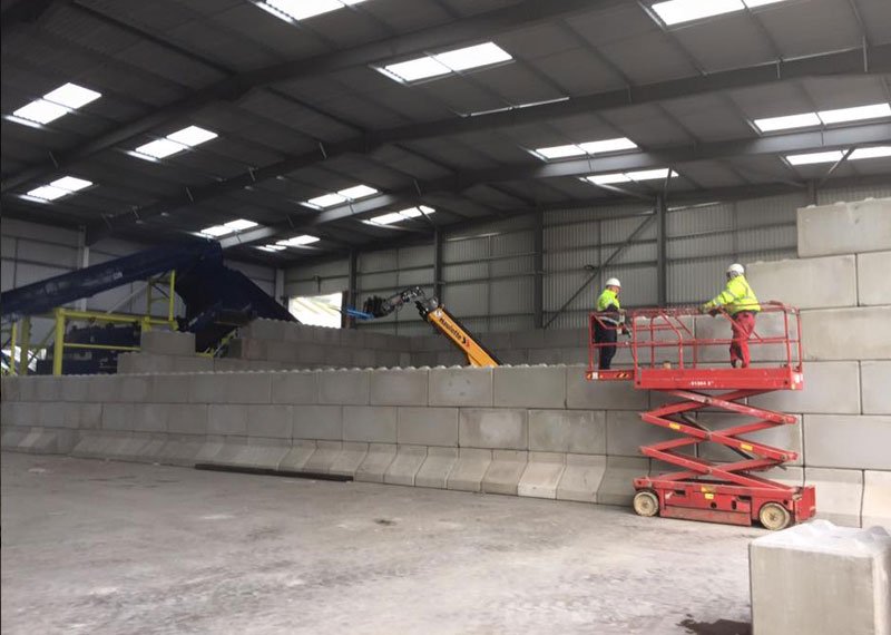 Workers on a scissor lift building block bay walls inside a recycling shed