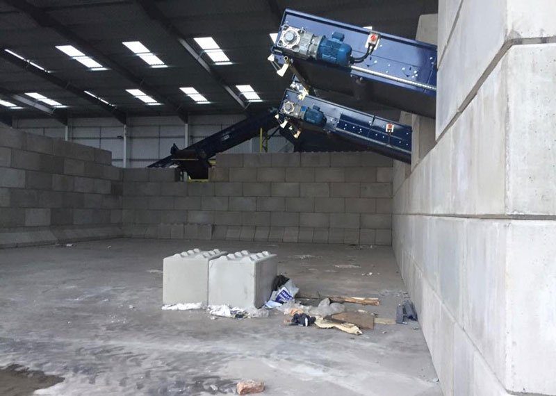 Interlocking block wall forming a storage bay beneath a conveyor inside a recycling building