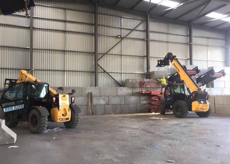 Telehandlers working beside an interlocking block storage bay wall inside a waste shed
