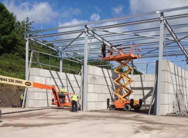 Steel frame being erected over Legato block storage bay walls with a scissor lift