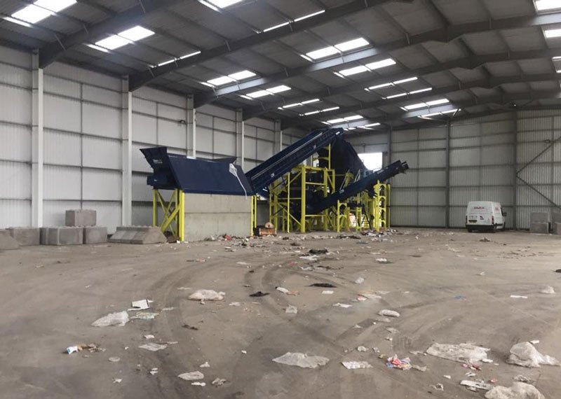 Empty waste transfer shed with a conveyor and litter across the concrete floor