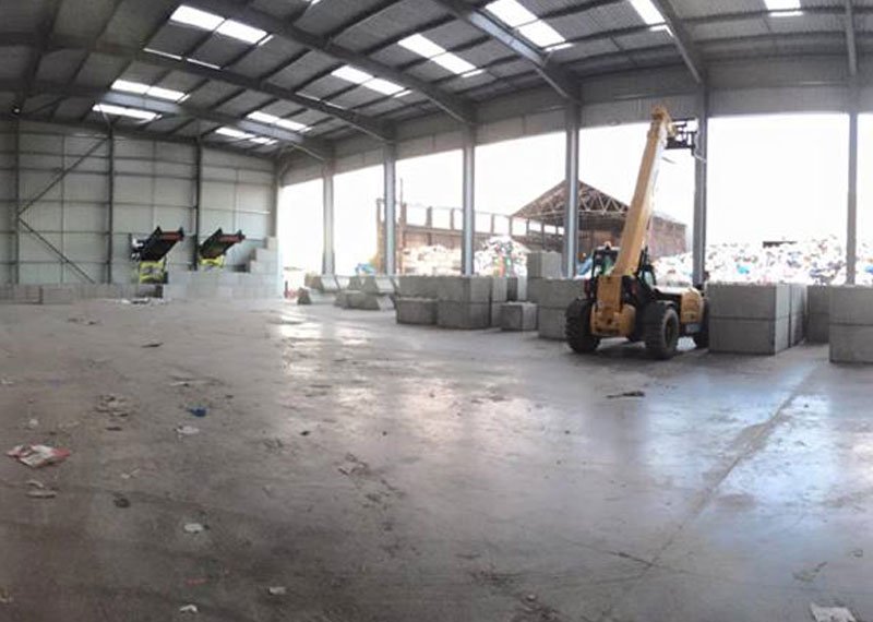 Telehandler moving Legato blocks in a waste facility beside open bays and a waste pile