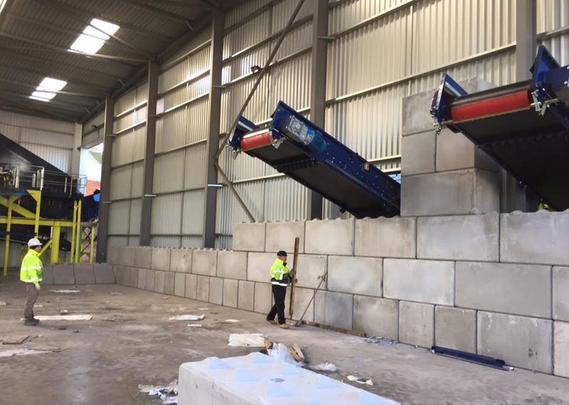 Workers building a Legato interlocking block wall beneath conveyors in a recycling shed