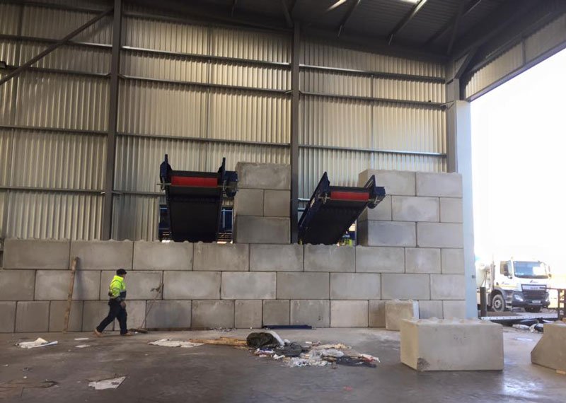 Worker walking past interlocking block bays beneath conveyor discharge points