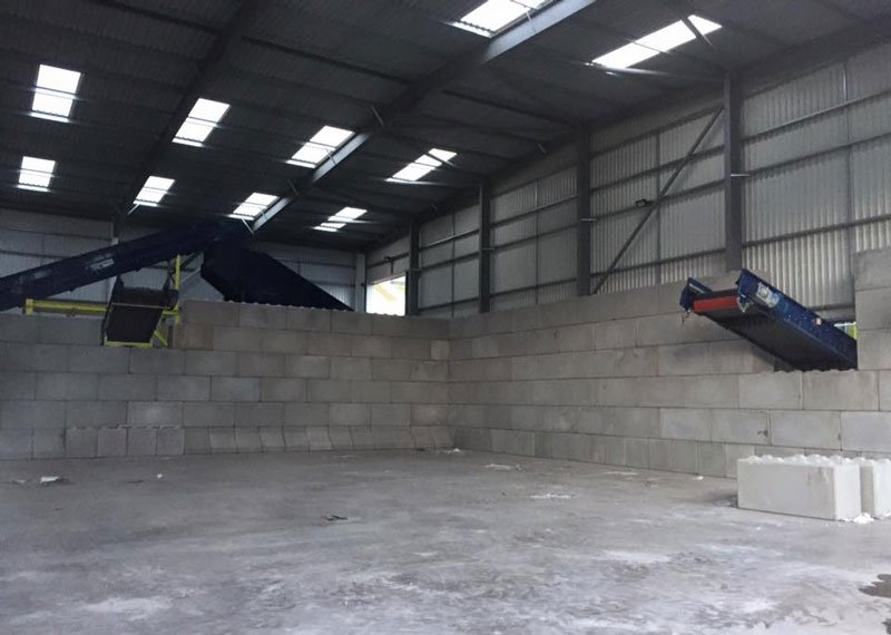 Conveyors overhanging interlocking block bay walls inside a waste facility