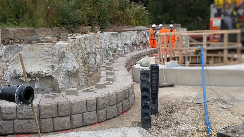 Curved Retainer-Rock cobblestone-finish wall under construction with drainage pipework behind