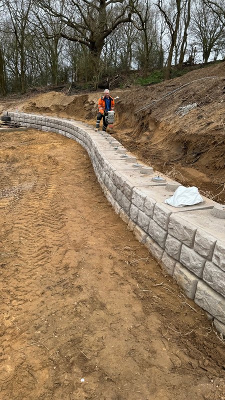 Worker installing curved Retainer-Rock walling along an excavated embankment