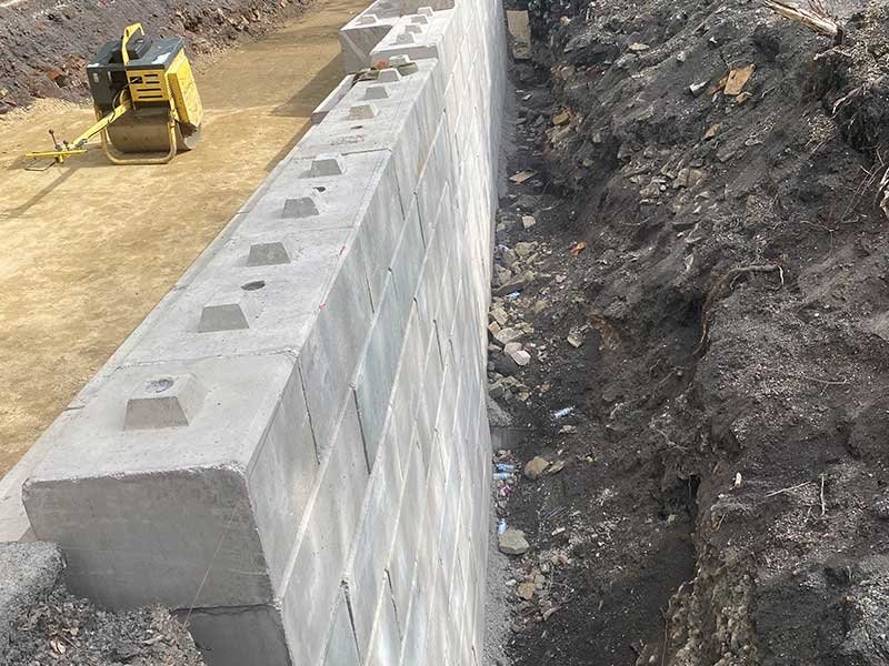 Duo block retaining wall built along an excavation with a compactor nearby