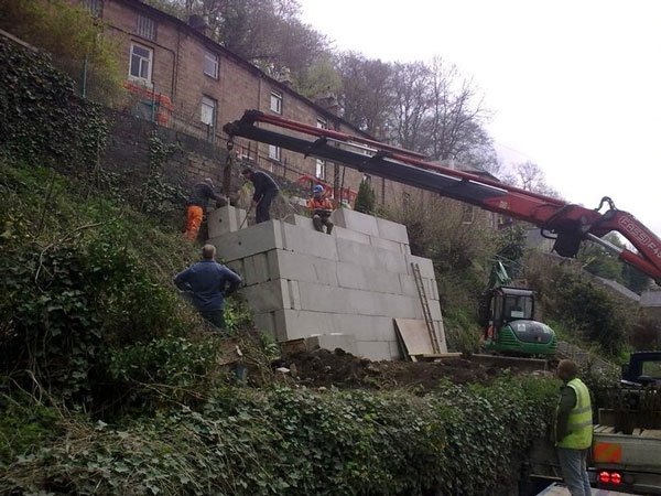 Workers and a lorry crane building block walling into a steep embankment