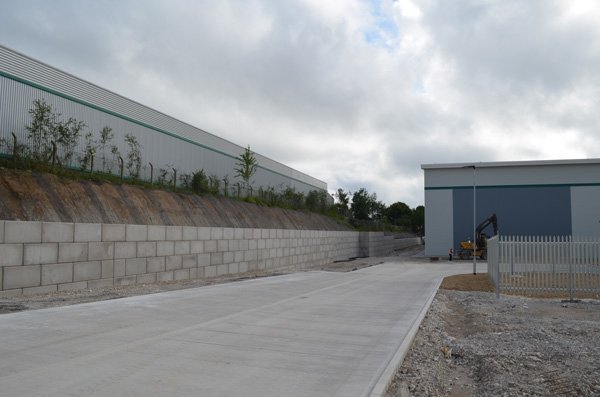 Interlocking block retaining wall running alongside a landscaped industrial park yard
