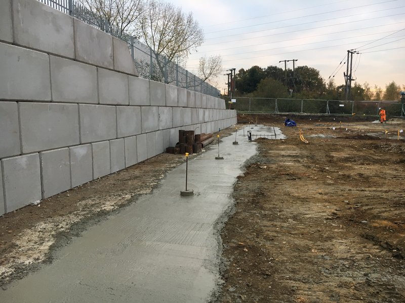 Legato retaining wall with fencing above and a new concrete slab at its base
