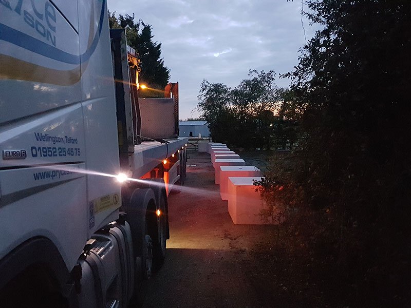 Lorry delivering security blocks along a roadside verge at dusk