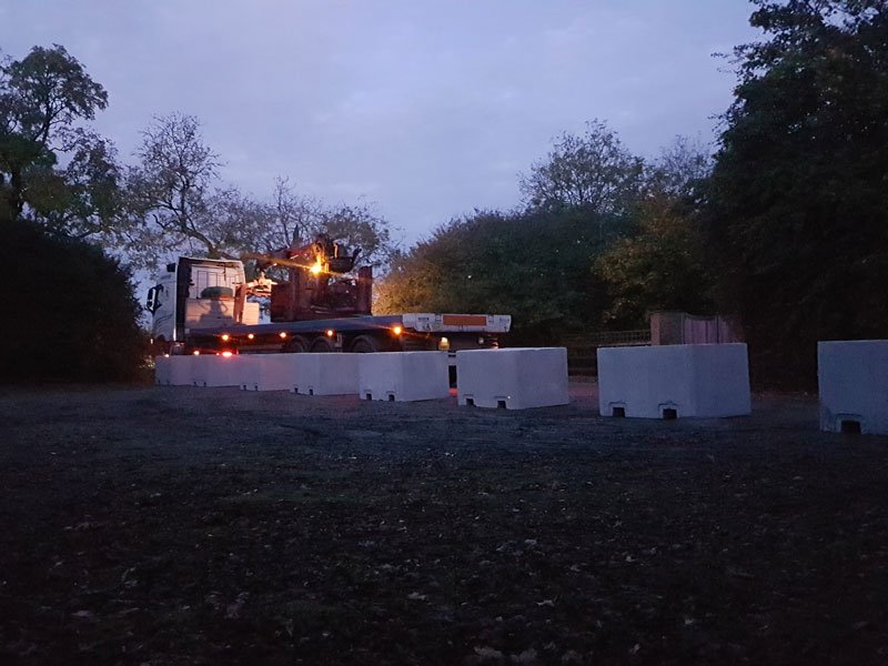 Security blocks placed across a field access with plant working at dusk