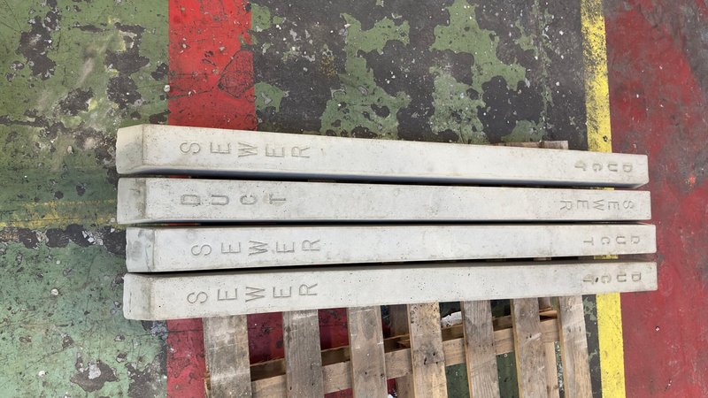 Sewer and duct indicator posts stacked on a timber pallet against a painted wall