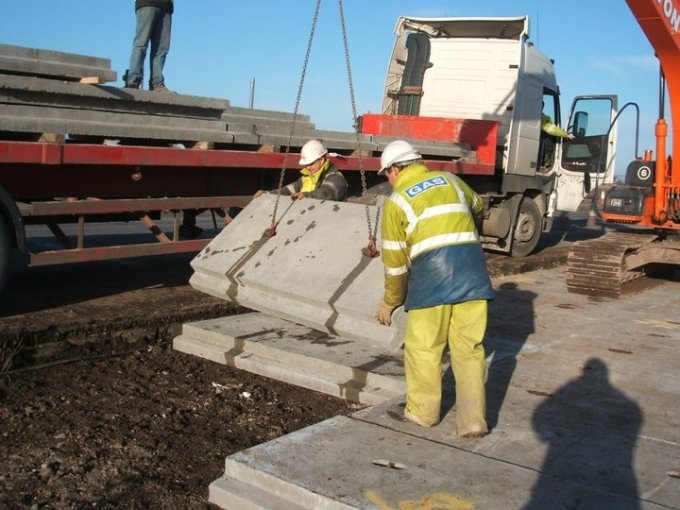 Worker guiding a precast utility protection slab lowered on chains into a trench