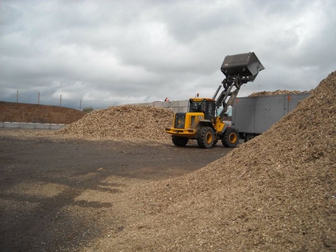 Loading shovel tipping woodchip beside an interlocking block storage bay wall