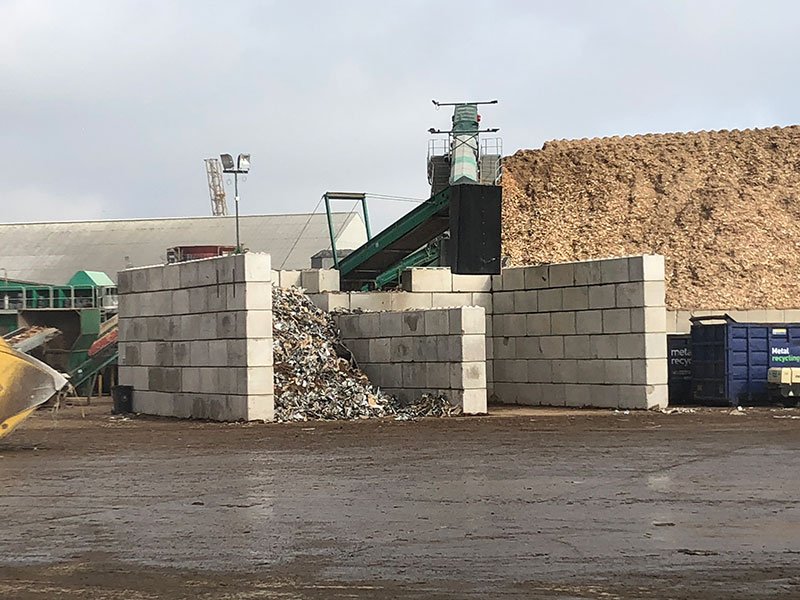 Legato interlocking blocks forming waste storage bays beside a conveyor and woodchip pile