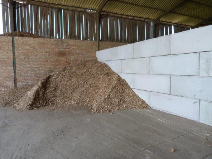 Woodchip heap stored against a white-painted interlocking block wall inside a barn