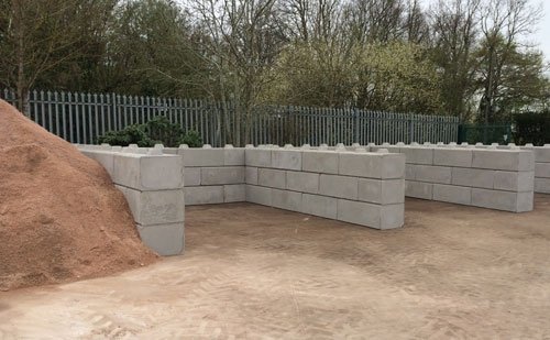 Duo interlocking block bay walls retaining a sand stockpile in a fenced yard