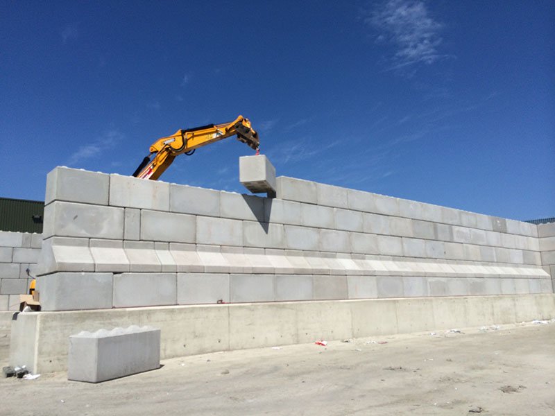 Excavator lifting a Legato block onto a newly built storage bay wall