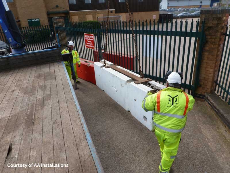 Workers in hi-vis guiding a TVCB barrier into place at a gated entrance