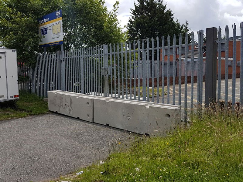 Line of temporary vertical concrete barriers set along a palisade-fenced boundary