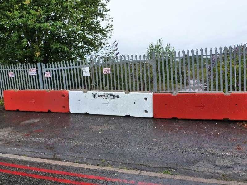 Red and white TVCB barriers lining a road beside a palisade fence