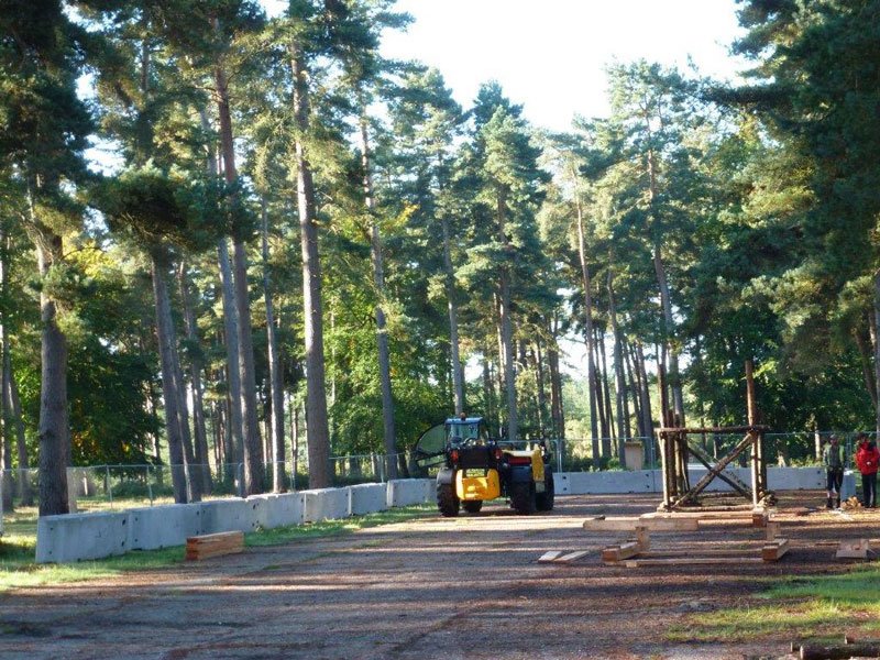 TVCB barriers being positioned by a telehandler among pine trees