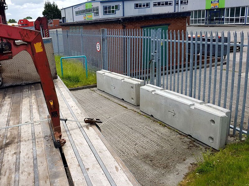 Temporary vertical concrete barriers being offloaded alongside a palisade fence