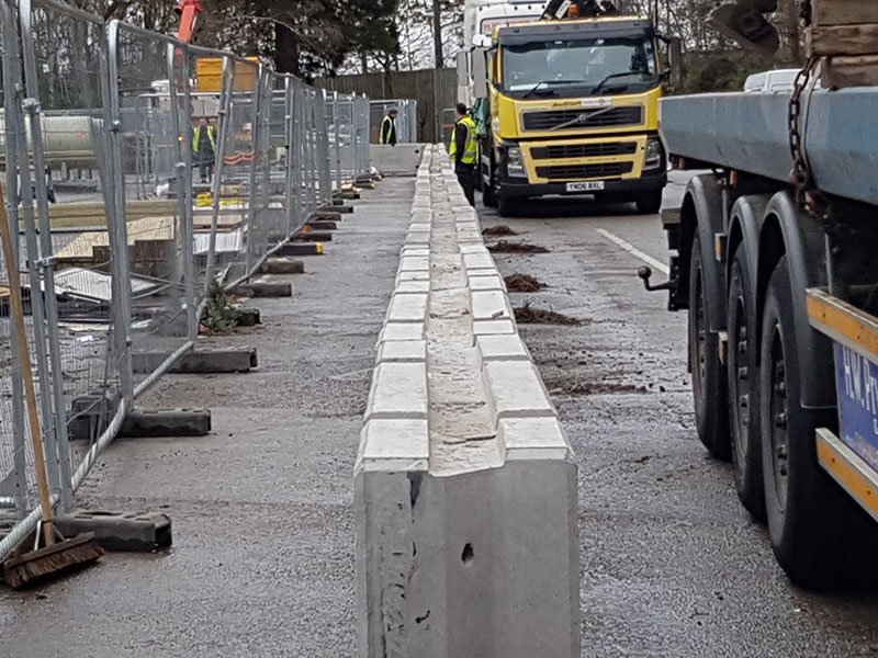 Temporary vertical concrete barriers being installed alongside a lorry and site fencing