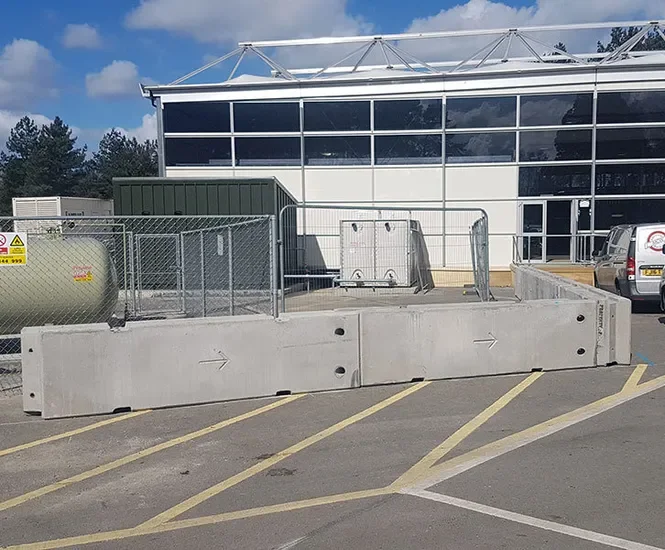 Temporary vertical concrete barriers protecting a fenced tank compound outside offices