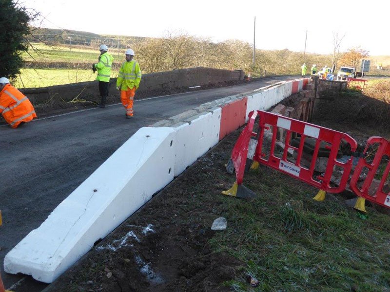 White temporary vertical concrete barrier edging a road repair with workers beyond