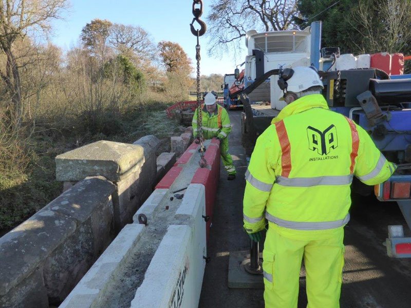 Workers installing temporary vertical concrete barriers along a bridge deck